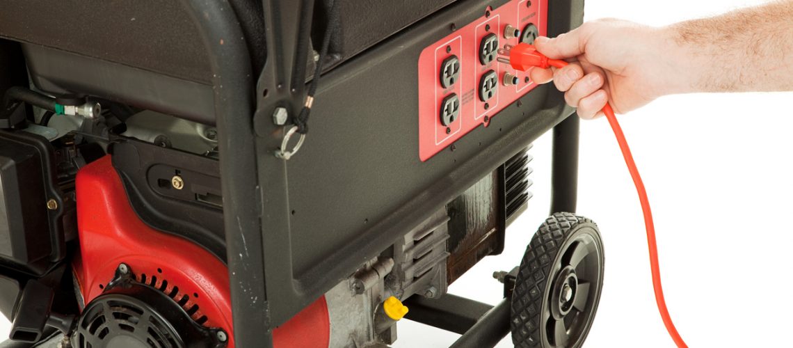 Plug In To Power Man's hand plugging an extension cord into an emergency generator.